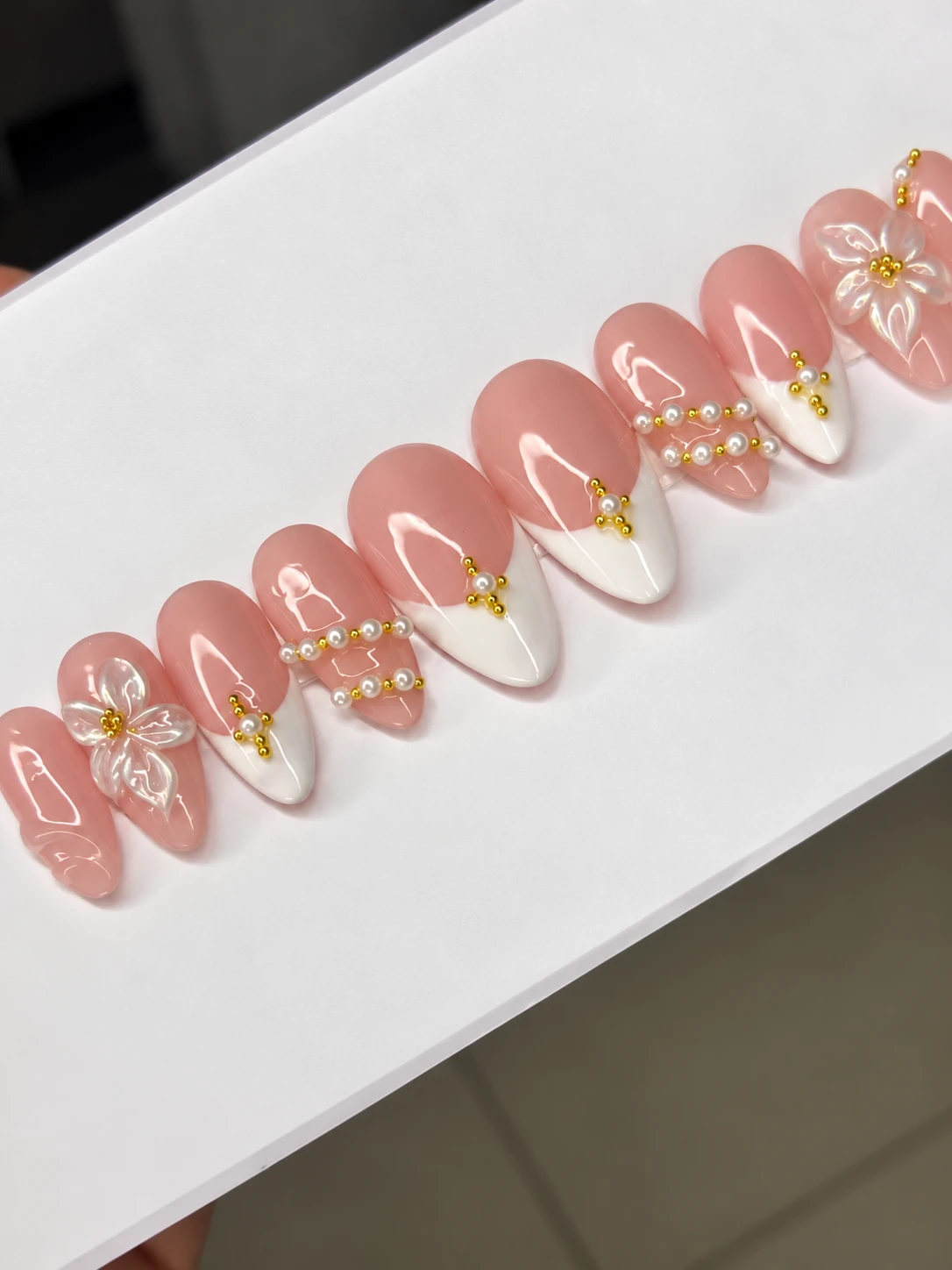 Pink French press-on nails decorated with pearls, gold beads and translucent flowers.